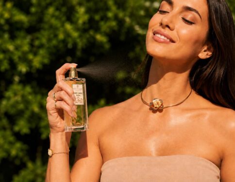 Parfum Ruby Chéri vaporisé par une femme souriante en extérieur, fragrance féminine raffinée aux notes gourmandes et florales.